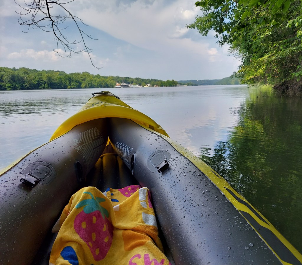 Lily sitting on a kayak on a river looking out onto the horizon.